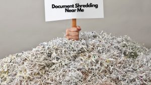 hand coming out of a pile of shredded paper that is holding a sign with the text "Document Shredding Near Me" on it