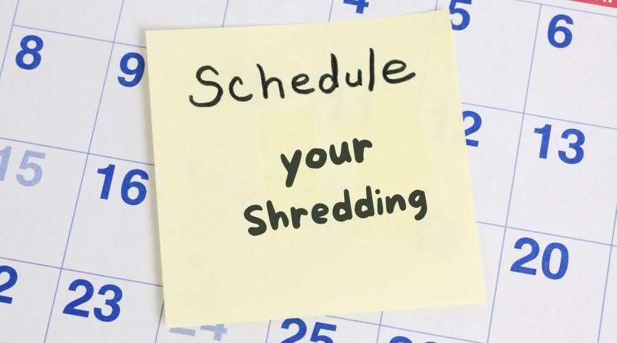 Post it note over a calendar that says "Schedule your shredding"